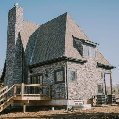 Rustic stone house with deck in rural setting.