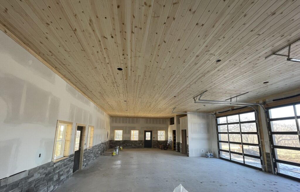Spacious unfinished garage with wooden ceiling and large windows.